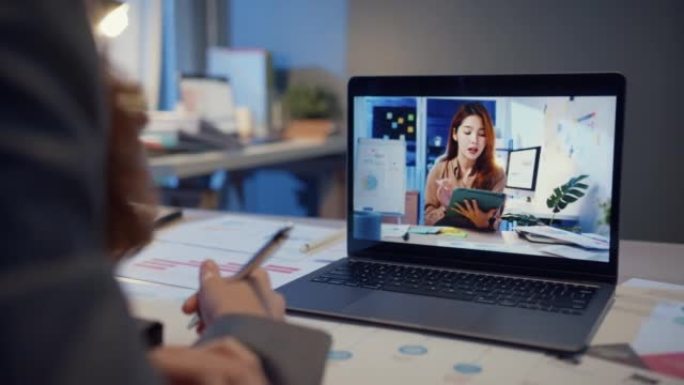 亚洲女商人使用笔记本电脑与同事讨论在家客厅视频通话会议的计划。夜间超负荷工作，远程，社交距离，检疫冠