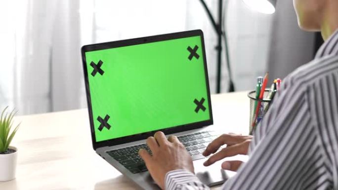 男人坐在带有绿色色度键屏幕的笔记本电脑前