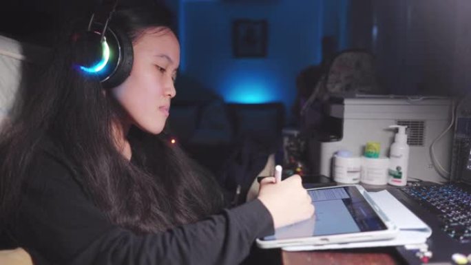 迷人的亚洲少女戴着耳机和老师在笔记本电脑上学习在线家庭学校，并在平板电脑上写作。视频通话学习作业
