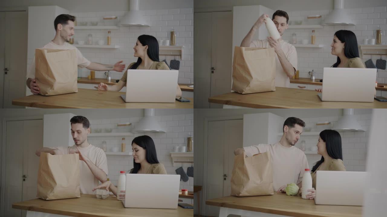 女人用笔记本电脑工作，而男人将杂货带到厨房并与妻子交谈时打开食物包装