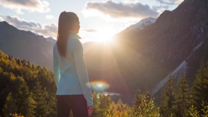 年轻的女徒步旅行者在日落时从山崖边缘欣赏山谷湖的壮丽景色