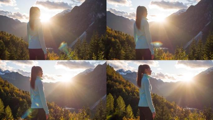 年轻的女徒步旅行者在日落时从山崖边缘欣赏山谷湖的壮丽景色