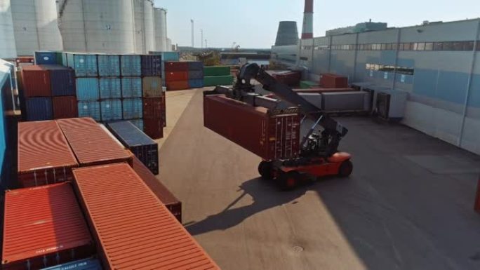 在造船厂码头中，一名集装箱搬运工在运送大型红色货运集装箱的空中无人机镜头。机器的驾驶员正在物流中心仓