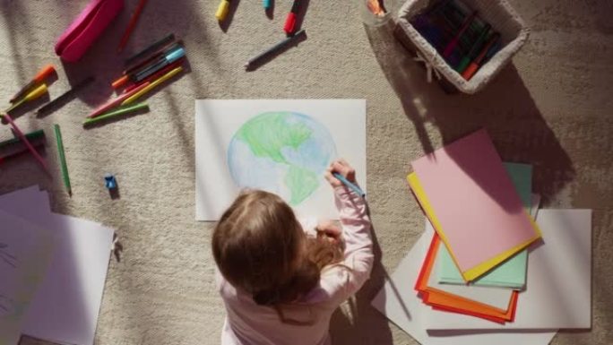 俯视图: 小女孩画我们美丽的地球。非常有才华的孩子在家里的地板上玩得开心，想象我们的家乡星球是一个快