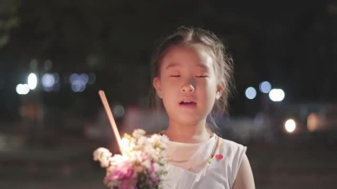 手里拿着花的亚洲小女孩晚上在寺庙里散步
