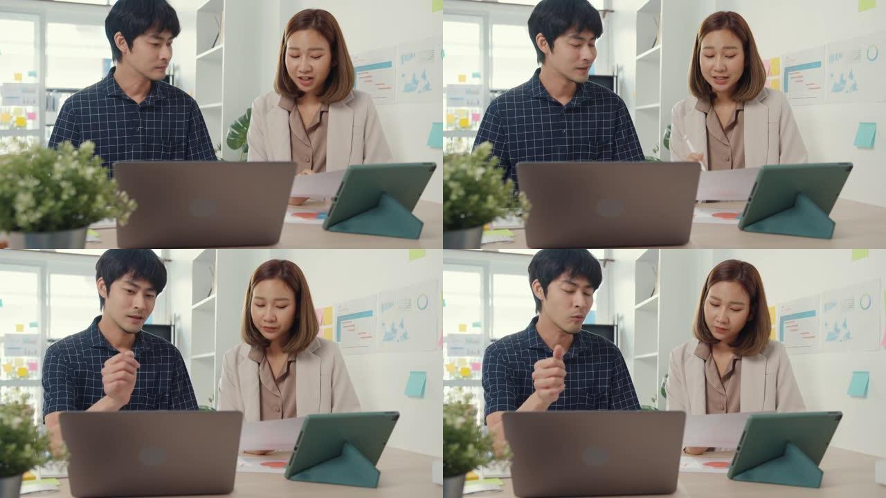 年轻的同事亚洲创意商人经理讨论项目比较在桌子上工作的文书工作和笔记本电脑的比较点，并坐在办公桌上一起