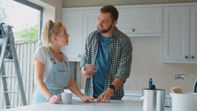 夫妇在家里装修厨房，在慢动作中看着咖啡休息时的油漆色板