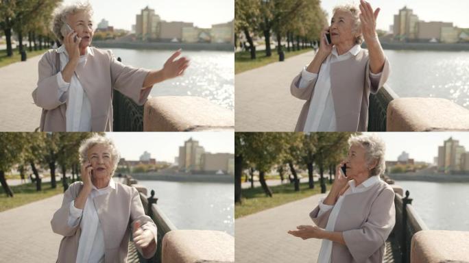 情绪激动的高级女士在手机上聊天并站在城市河边打手势的肖像