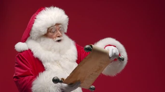 一个微笑的圣诞老人打开纸卷，阅读并微笑，对他所读的内容感到满意，站在红色背景上