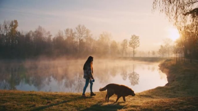 年轻女子带着她的狗沿着雾湖散步
