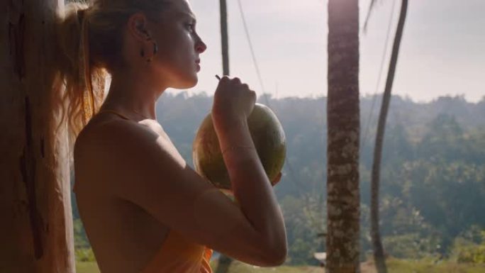 年轻的旅游女人在热带酒店度假胜地喝椰子鸡尾酒，看着美丽的丛林景色，享受天堂里异国情调的度假生活方式