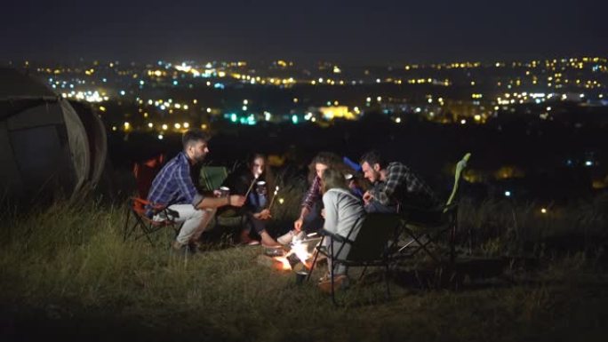 人们在夜城背景下的帐篷附近坐着聊天