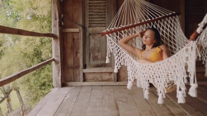 吊床上的性感女人在度假胜地享受舒适的生活方式，在热带天堂小屋的慵懒夏日平静地摇摆