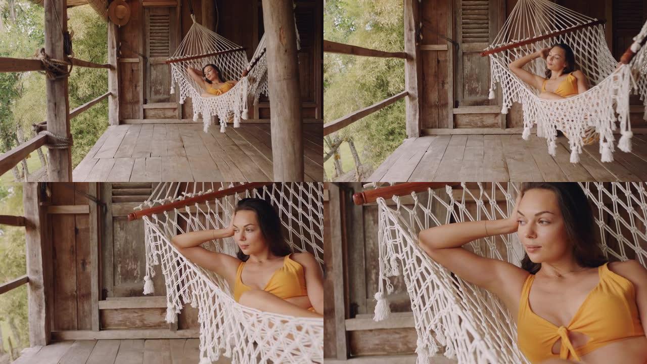 吊床上的性感女人在度假胜地享受舒适的生活方式，在热带天堂小屋的慵懒夏日平静地摇摆