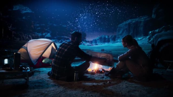 幸福的夫妇晚上一起在峡谷荒野露营，坐在篝火旁，用地图计划徒步旅行。两个旅行徒步旅行者交谈，银河之星观