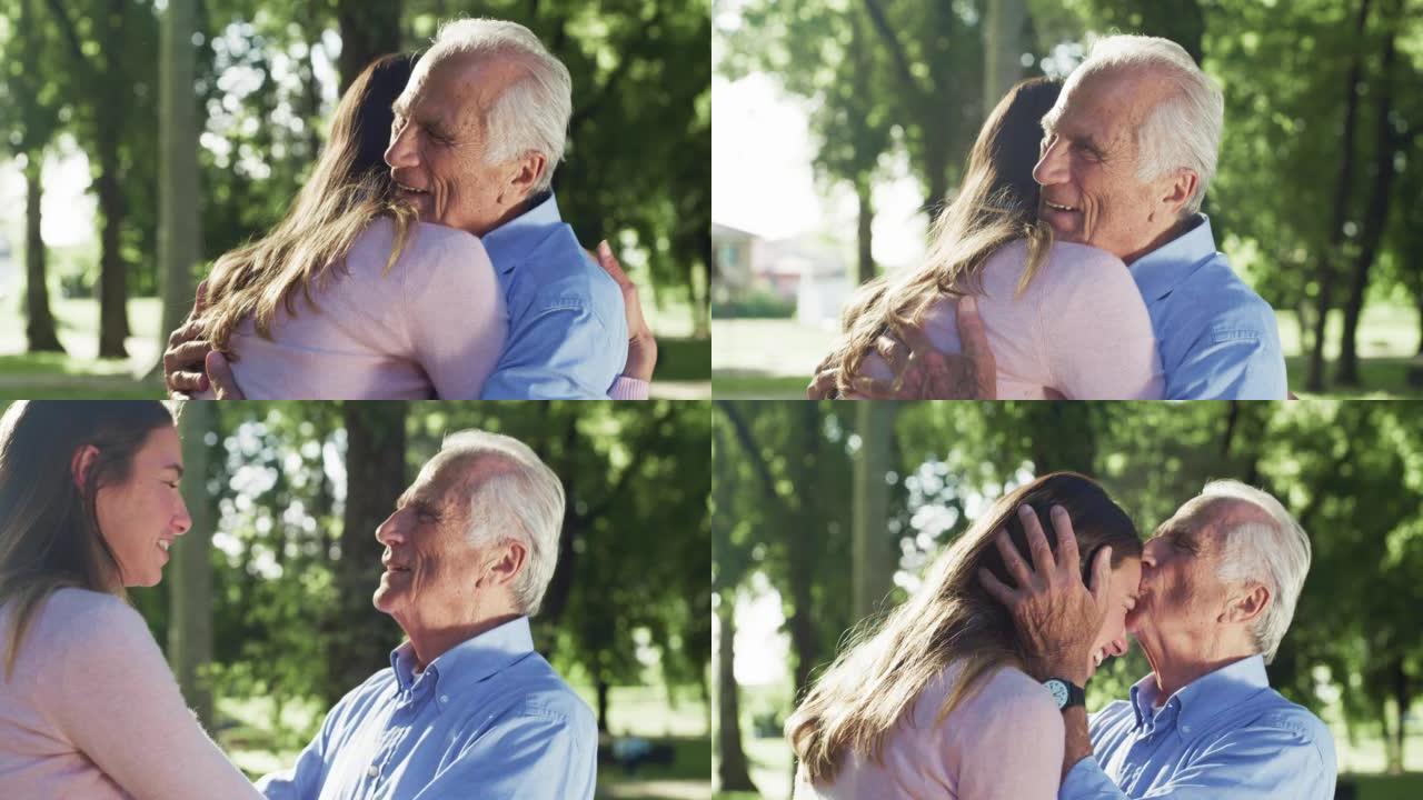 在阳光明媚的日子里，在绿色公园，电影拍摄的快乐孙女给祖父一个情感的拥抱，以示爱和尊重。生活观念，祖父