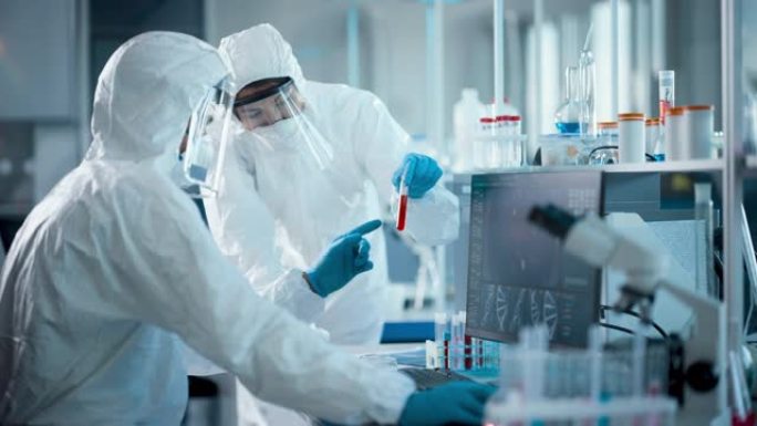 医学实验室: 微生物科学家团队穿着无菌工作服，面罩和口罩交谈，使用计算机分析血液样本并开发疫苗，药物