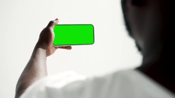 年轻人使用带有绿屏色度键特写的智能手机。家伙看起来拿着手机模型。概念观看和展示互联网社交媒体，视频通