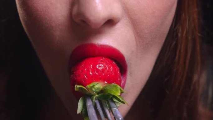 年轻女子的嘴在银叉子上咬草莓
