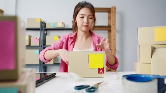 年轻的亚洲企业家商人包装产品在纸箱中交付给客户，在家庭办公室工作。