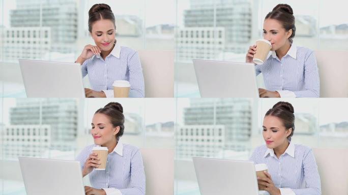 年轻的女商人在笔记本电脑上喝咖啡
