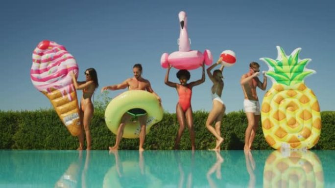 穿着泳装的年轻多民族朋友在阳光明媚的日子里，在游泳池里享受着他们的暑假，那里有五颜六色的充气用品