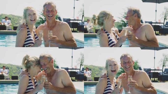 暑假在游泳池放松的高级夫妇的肖像用香槟庆祝