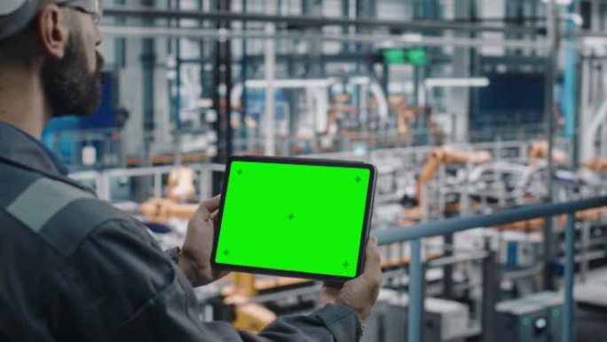汽车工厂工程师在工作制服中使用带有绿屏模型显示的平板电脑。汽车工业制造工厂从事汽车生产的增强现实软件