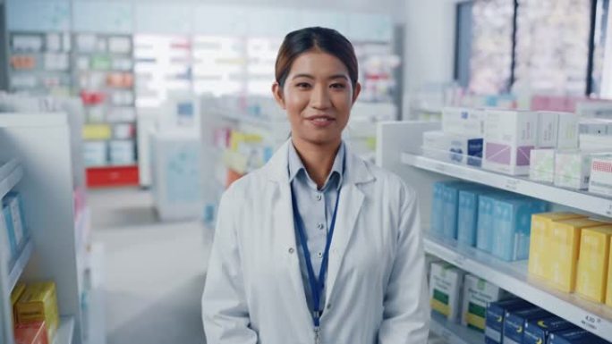 药房药店: 美丽的亚洲药剂师穿着白色外套，看着相机，迷人地微笑着，她的架子后面摆满了药品包装。中特写