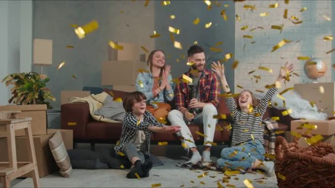 有两个孩子的年轻幸福家庭坐在沙发上庆祝购买，用五彩纸屑大炮搬进新公寓。