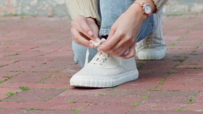 女人的手将鞋子或运动鞋绑在人行道上，开始或准备在城镇或城市中行走。休闲女性的鞋带或鞋类被绑住或系好以
