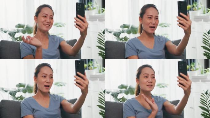 特写镜头年轻的亚洲女性在沙发上休闲穿着使用智能手机举起手视频通话打招呼，并在客厅室内植物中与家人和朋