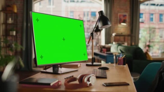 台式电脑，模拟绿屏显示站在舒适的客厅的桌子上。在背景中，时尚的现代明亮的家庭办公室工作室白天有大的城