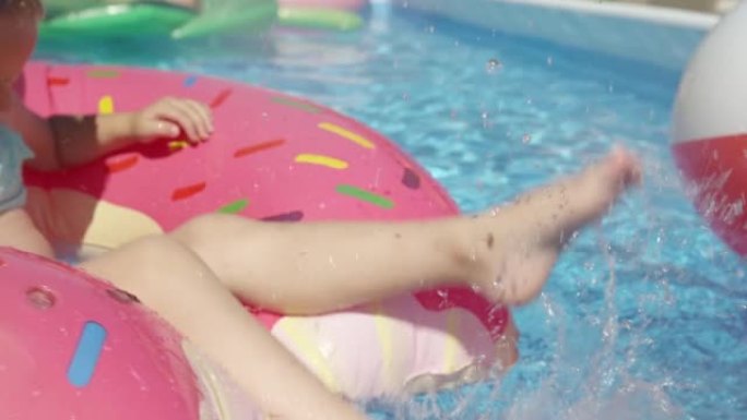 特写: 女婴的腿从游泳池中的漂浮甜甜圈中泼水