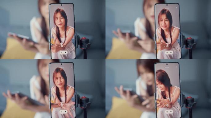 快乐年轻的亚洲女孩博客在手机摄像头前使用平板电脑在家里的客厅享受与追随者的问题答案。博客活动生活方式