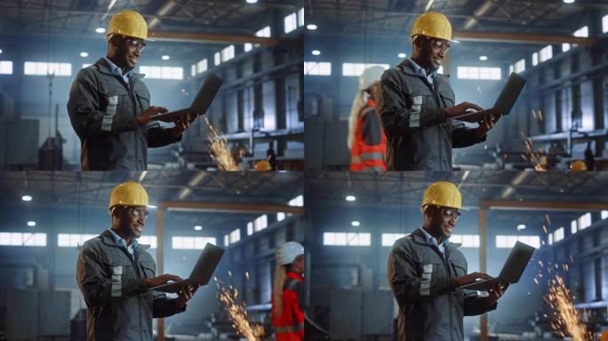 专业重工业工程师/穿着安全制服和安全帽的工人使用笔记本电脑。微笑的非洲裔美国工业专家站在金属建筑制造