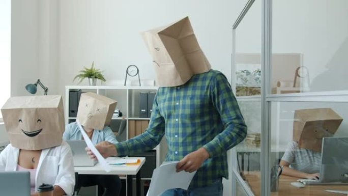 办公室工作人员的纸袋头显示表情符号在办公桌上的项目中工作，而脾气暴躁的老板在给文件
