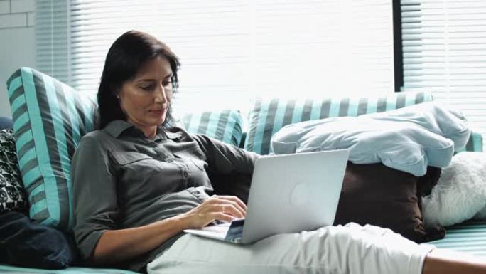 女人坐在沙发上在家使用笔记本电脑