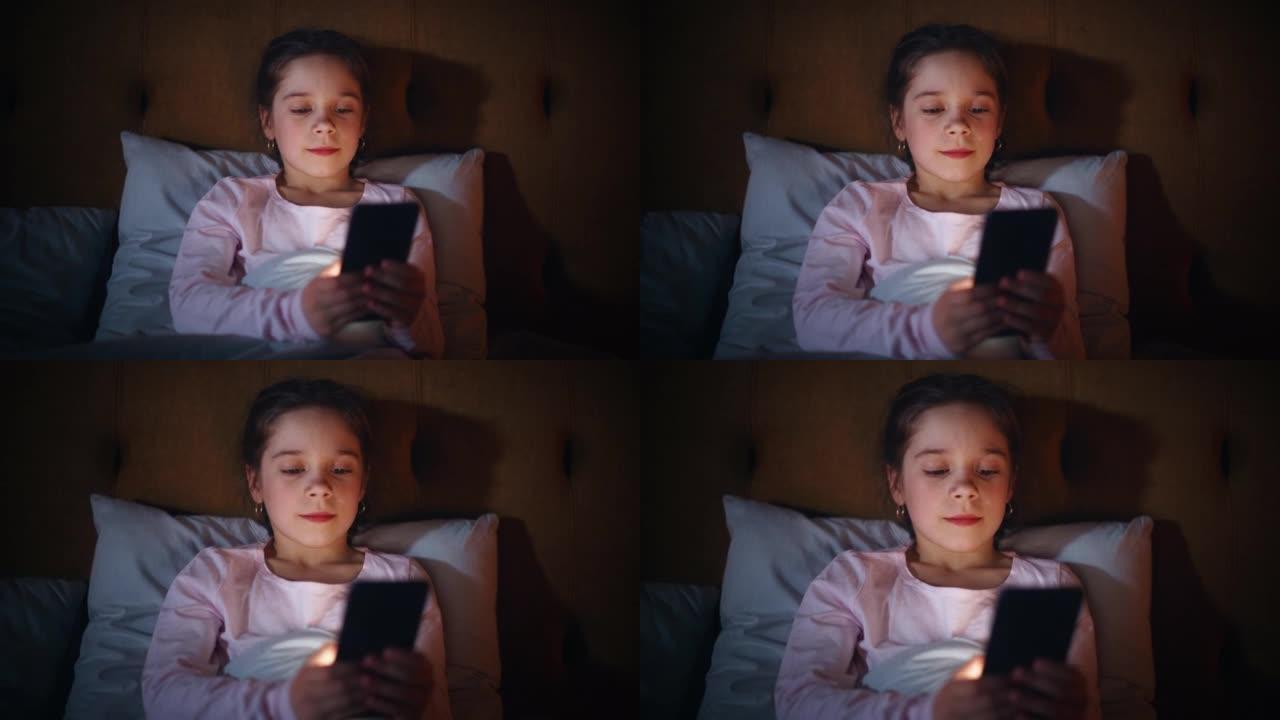 小女孩睡觉前在床上使用智能手机。可爱的孩子检查社交媒体，学校时间表，在数字电子书上阅读作业，与朋友在
