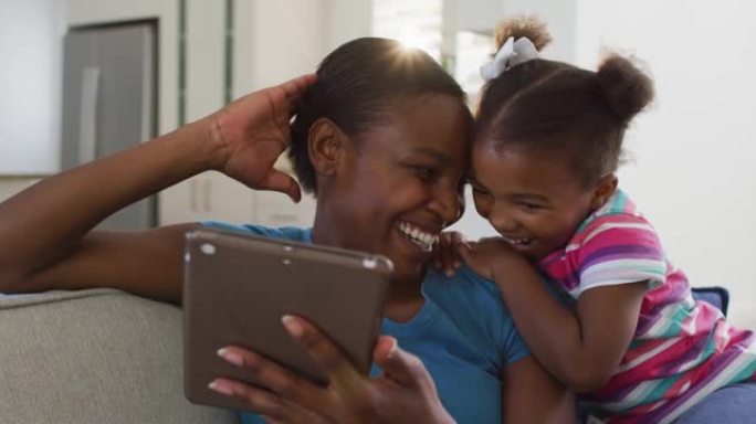 快乐的非洲裔美国母女坐在沙发上使用数字平板电脑笑着