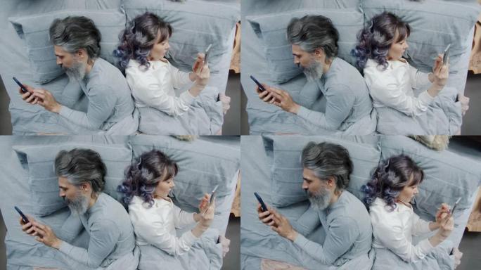 男人和女人背靠背躺在床上，使用智能手机享受小工具