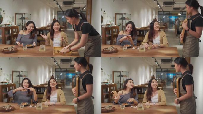 亚洲华人女服务员从厨房柜台接管托盘上的食物，在餐厅为她的2位女性顾客服务