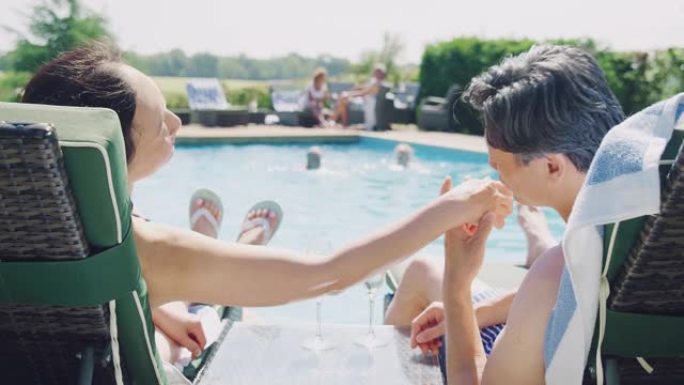 暑假在游泳池边放松的躺椅上的成熟夫妇喝香槟