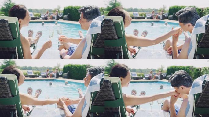 暑假在游泳池边放松的躺椅上的成熟夫妇喝香槟