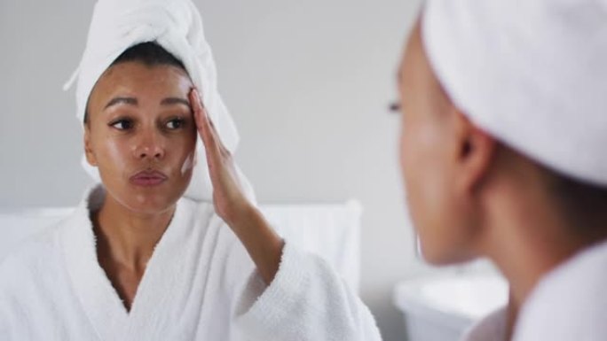 穿着浴袍的非裔美国妇女在浴室照镜子涂面霜