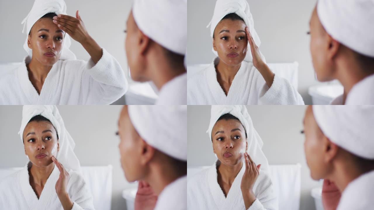 穿着浴袍的非裔美国妇女在浴室照镜子涂面霜