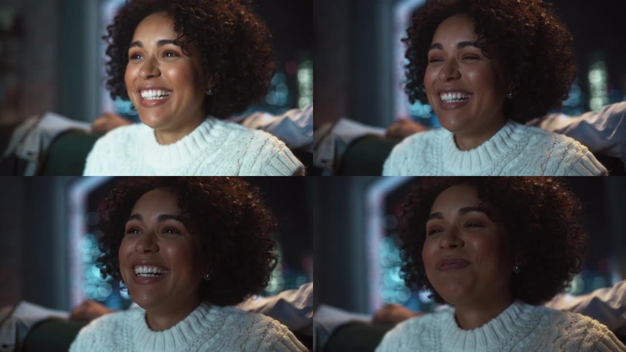 黑人女性在晚上在电视上看喜剧时大声大笑。具有积极情绪的多样化女人的肖像。特写