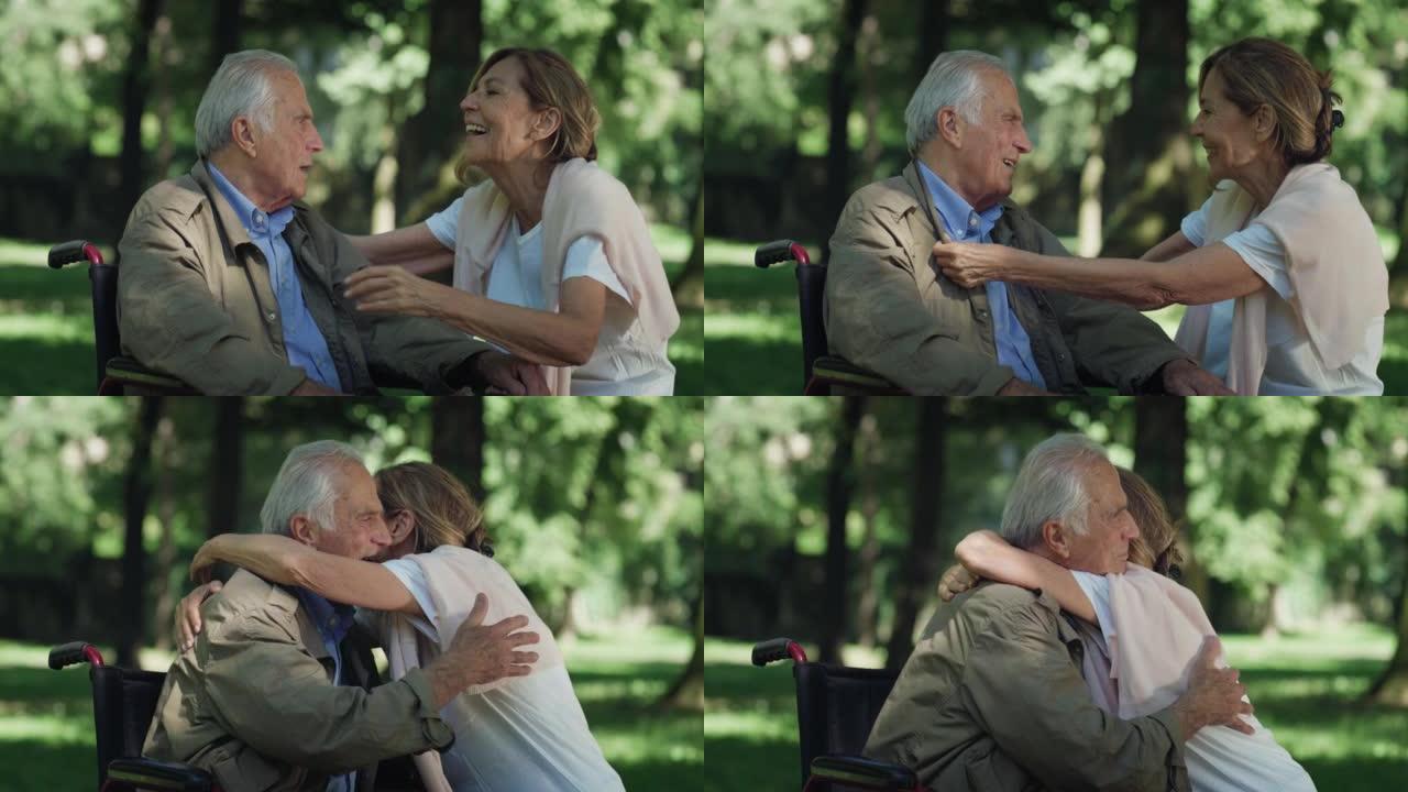 快乐微笑的成熟妻子的电影镜头正在给情感拥抱，让坐在轮椅上的丈夫残疾，这是绿色公园永远永恒爱情的标志。