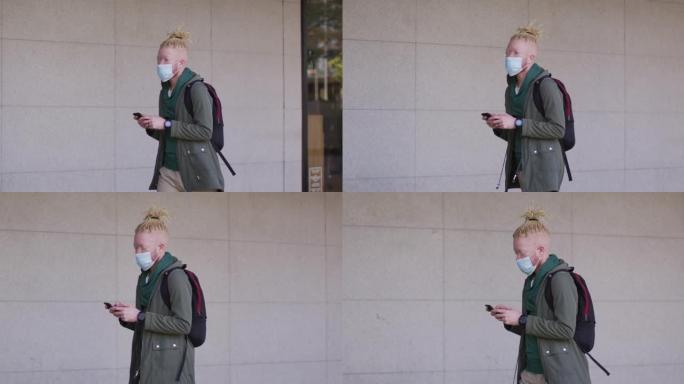 白化非裔美国男子戴着口罩和辫子走路和使用智能手机