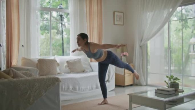 年轻的亚洲妇女在家在客厅练习瑜伽